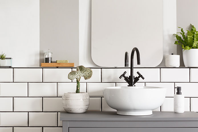 Real photo of a sink on a cupbaord in a bathroom interior with tiles, mirror and plants