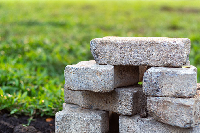 A stack of grey, rectangular paving stones sits on a bright green lawn.