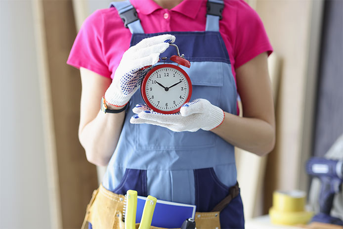 Close-up of woman worker in uniform holding red clock reminder to finish work on time.